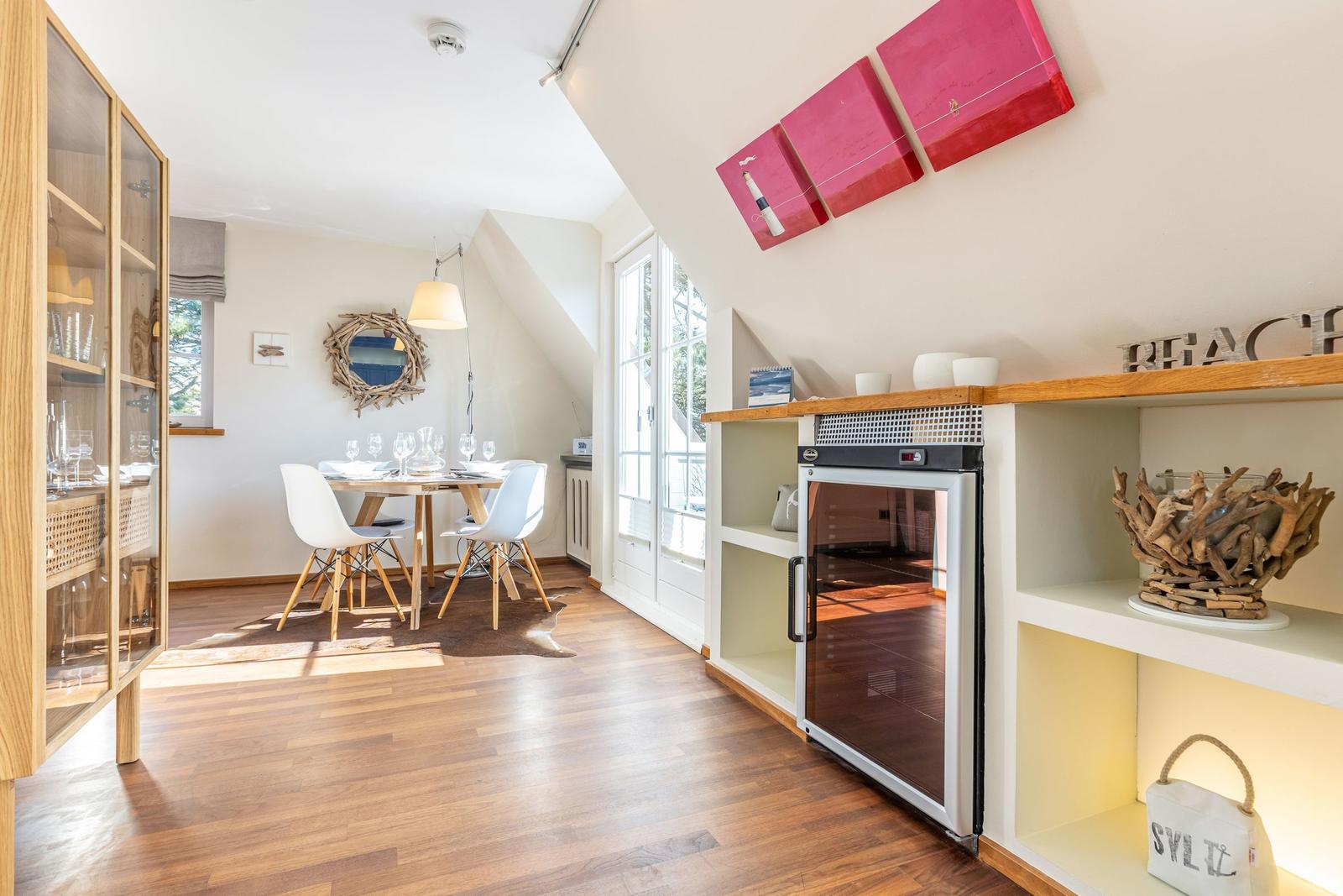 Esszimmer mit Tisch, Stühlen und Kühlschrank. Holzboden und Fenster.