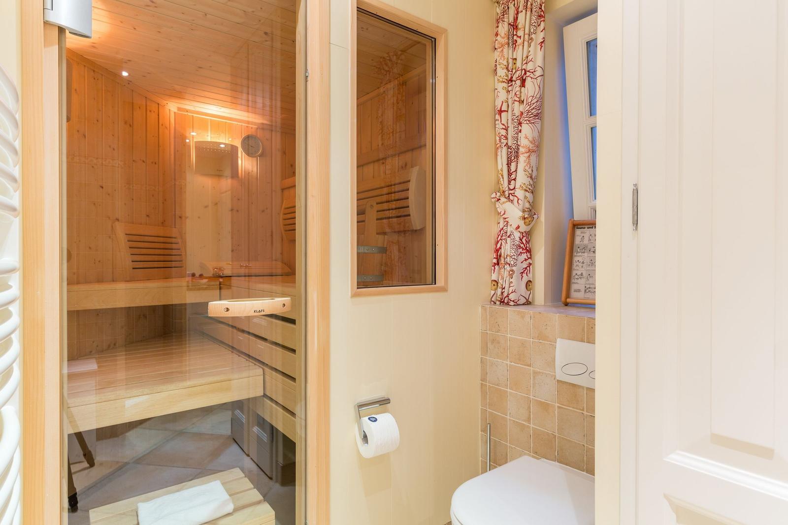 Sauna with wooden bench and glass wall, next to toilet and window with curtain.