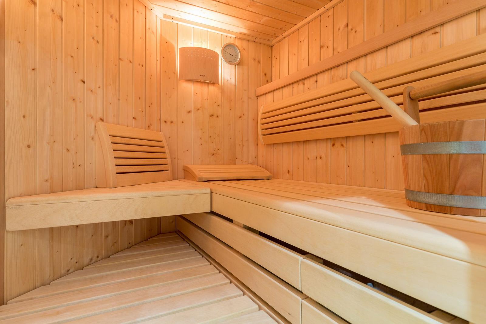 Sauna with wooden bench, wooden bucket, and thermometer on the wall.