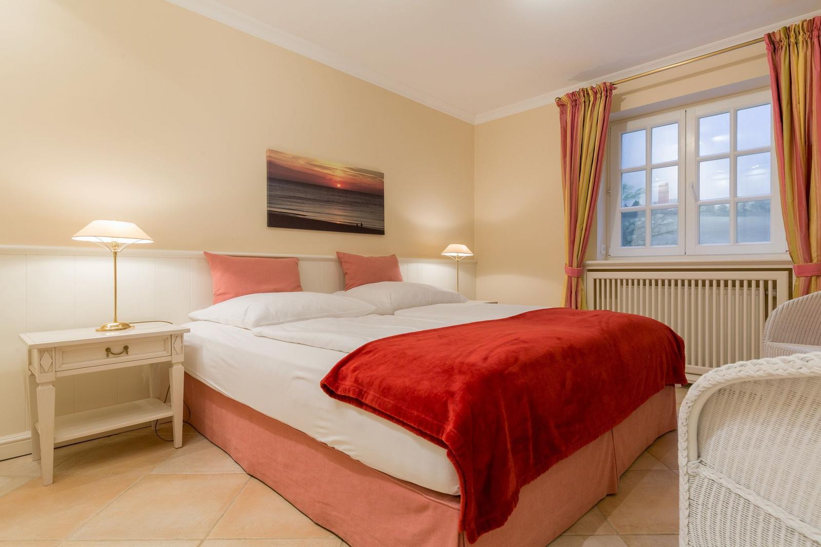 Bedroom with double bed, nightstand, window, and wall art.