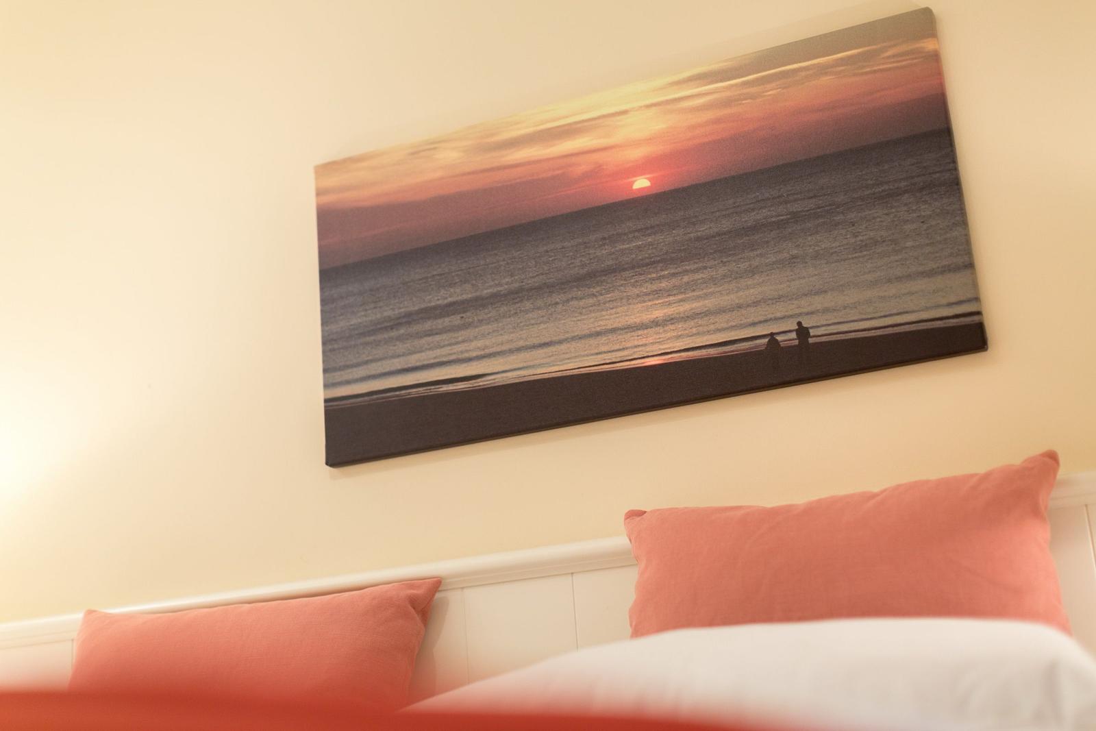 Bed with pillows under wall picture of sunset at beach