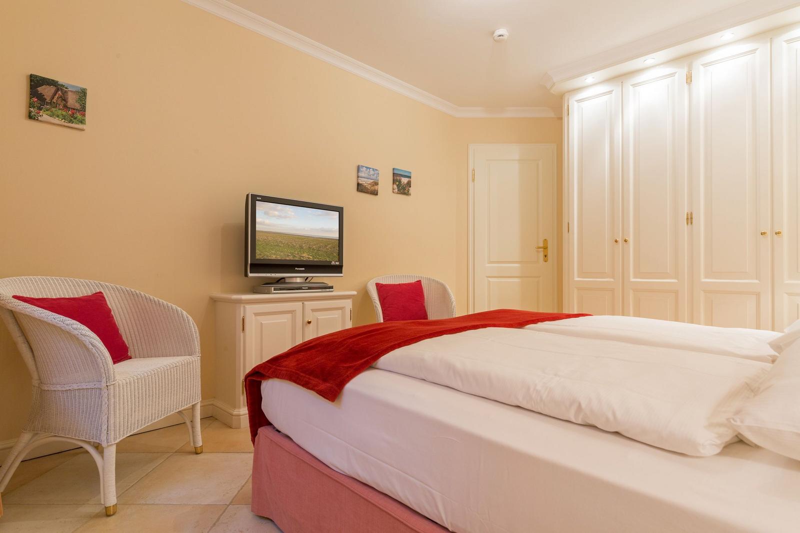 Bedroom with double bed, TV, white chairs, and wardrobe.