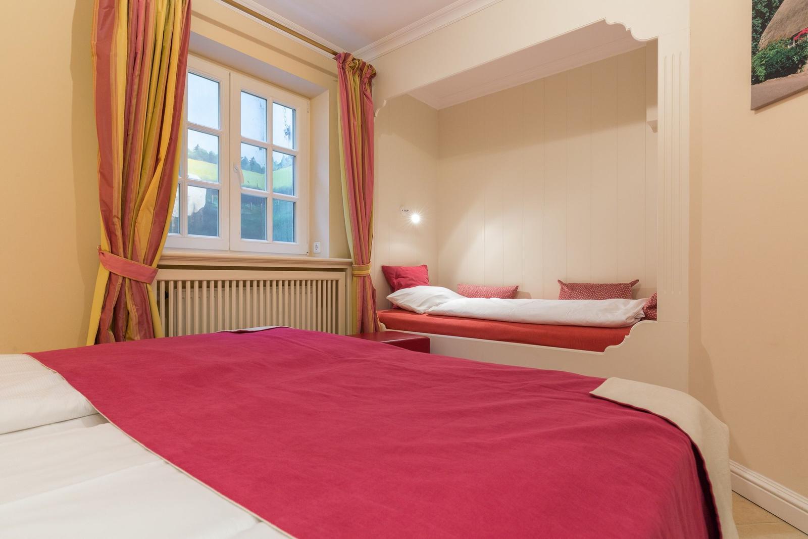 Bedroom with large bed and small bed in recessed area.