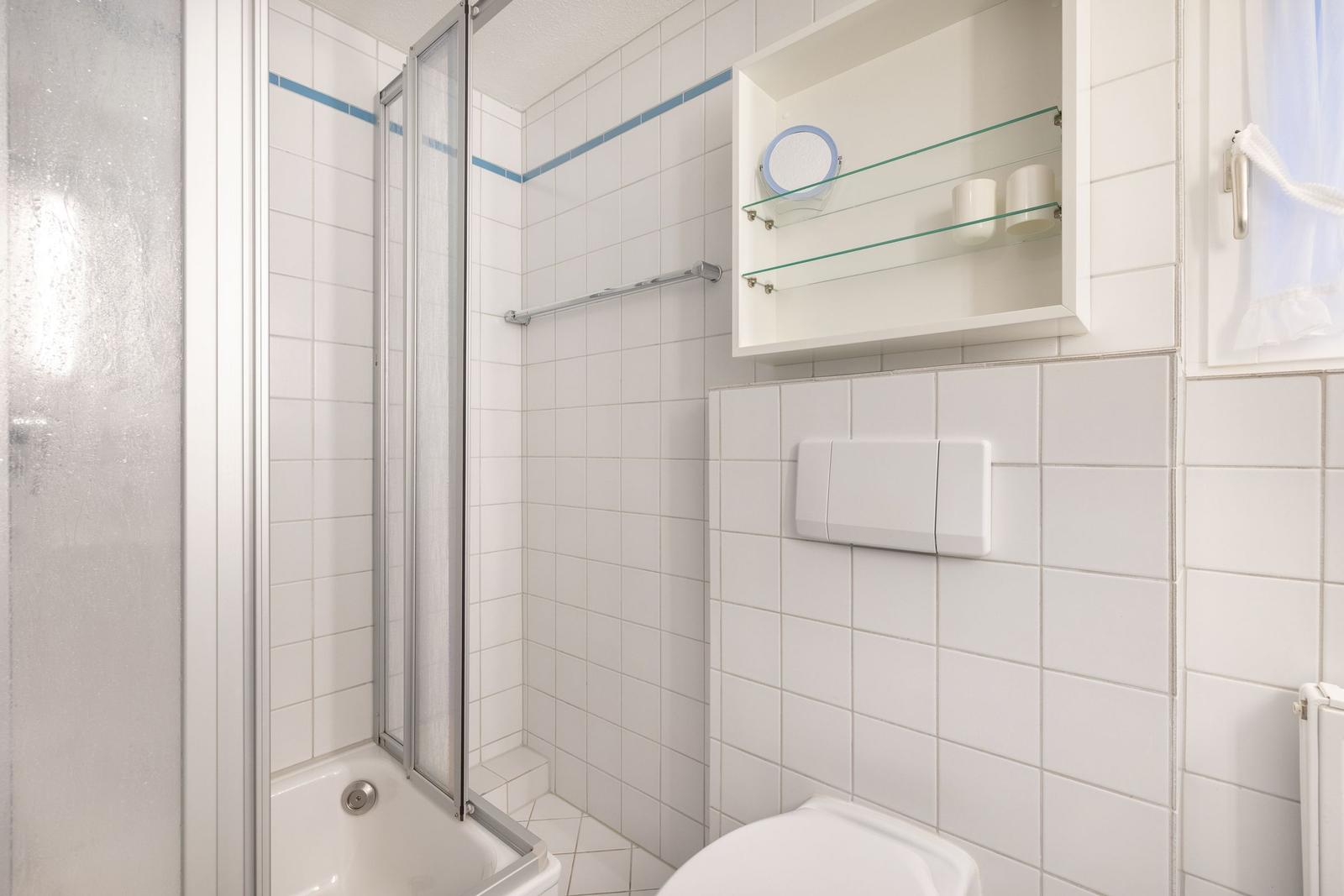 Badezimmer mit Dusche, Toilette und Aufbewahrungskasten an der Wand.
