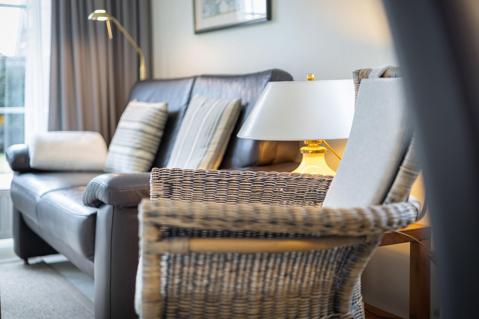 Ein Wohnzimmer mit Ledersofa, Kissen und einem Stuhl mit geflochtenem Sitz.