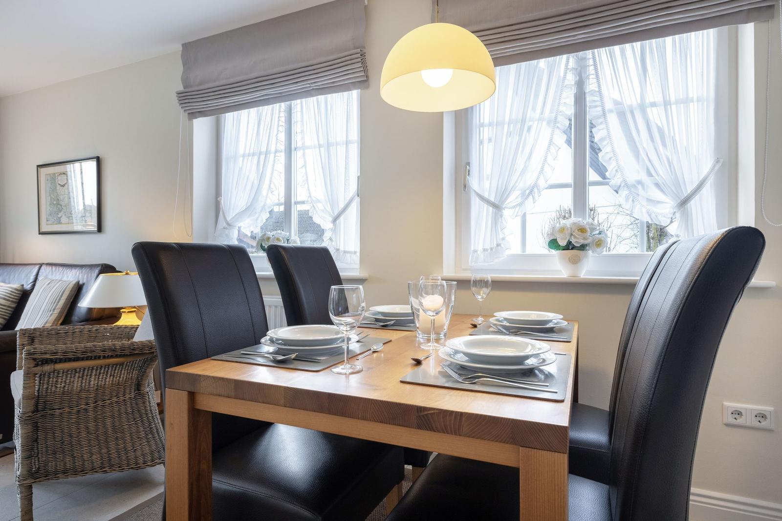 Esszimmer mit Holztisch, schwarzen Stühlen und Fenstern mit weißen Vorhängen.