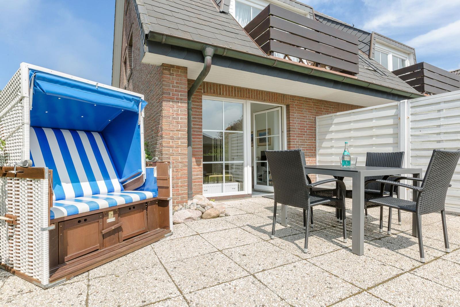 Terrasse mit Strandkorb und Tisch mit Stühlen vor einem Haus