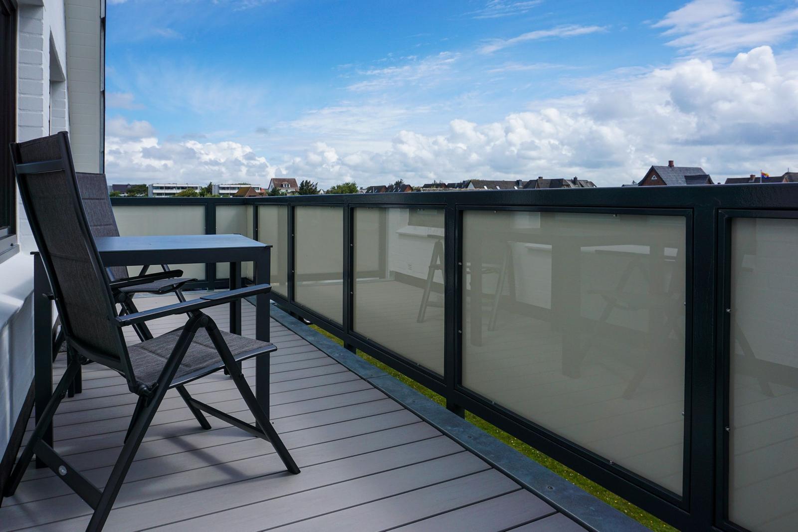 Terrace with table, chairs, and privacy screen. View of residential area under blue sky.