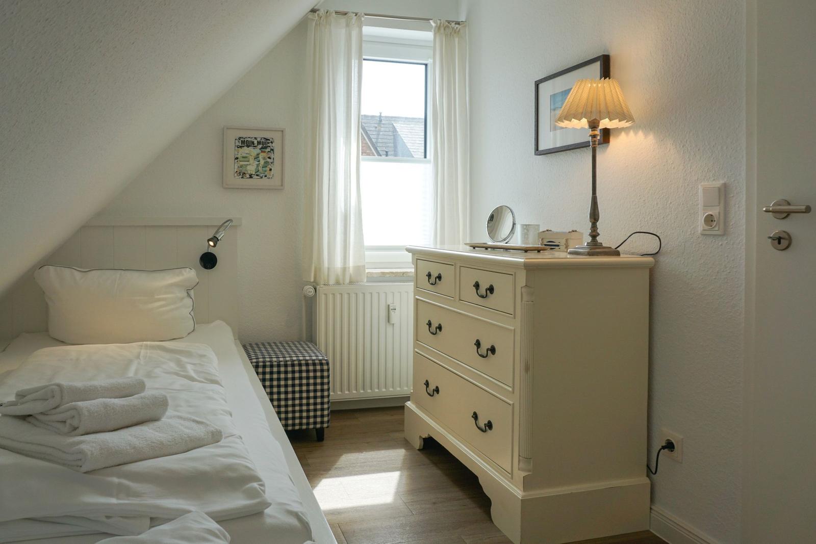 Bedroom with sloped ceiling, bed, dresser, and window with curtains.