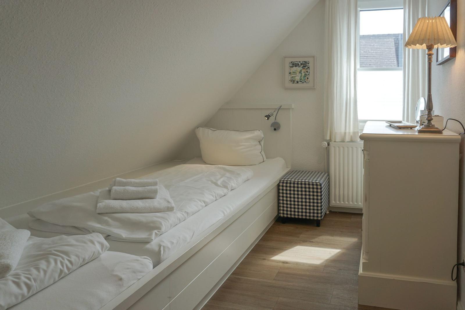 A bedroom with sloped ceiling, bed, dresser, and window.