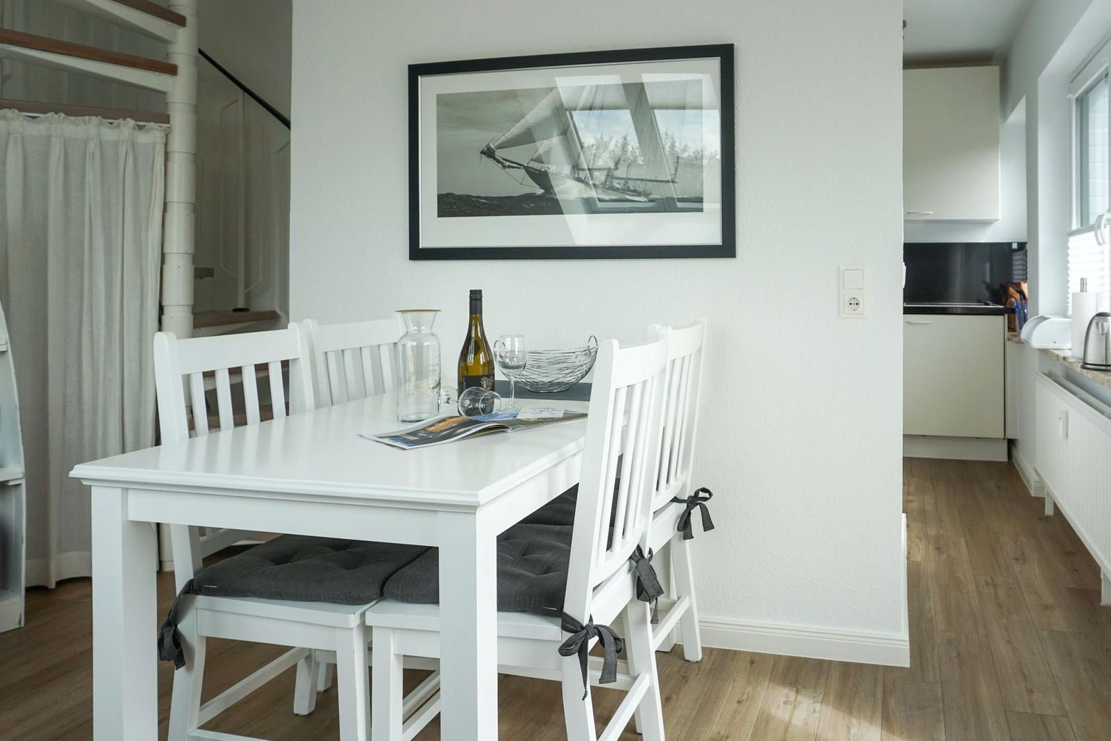 Dining room with white table and chairs, wall picture, and kitchen area in background.