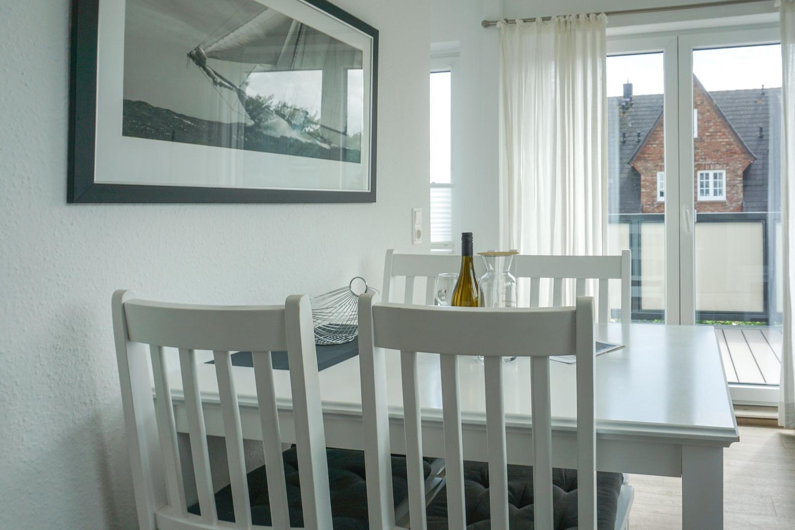 Dining area with white table and chairs, window overlooking balcony and house.