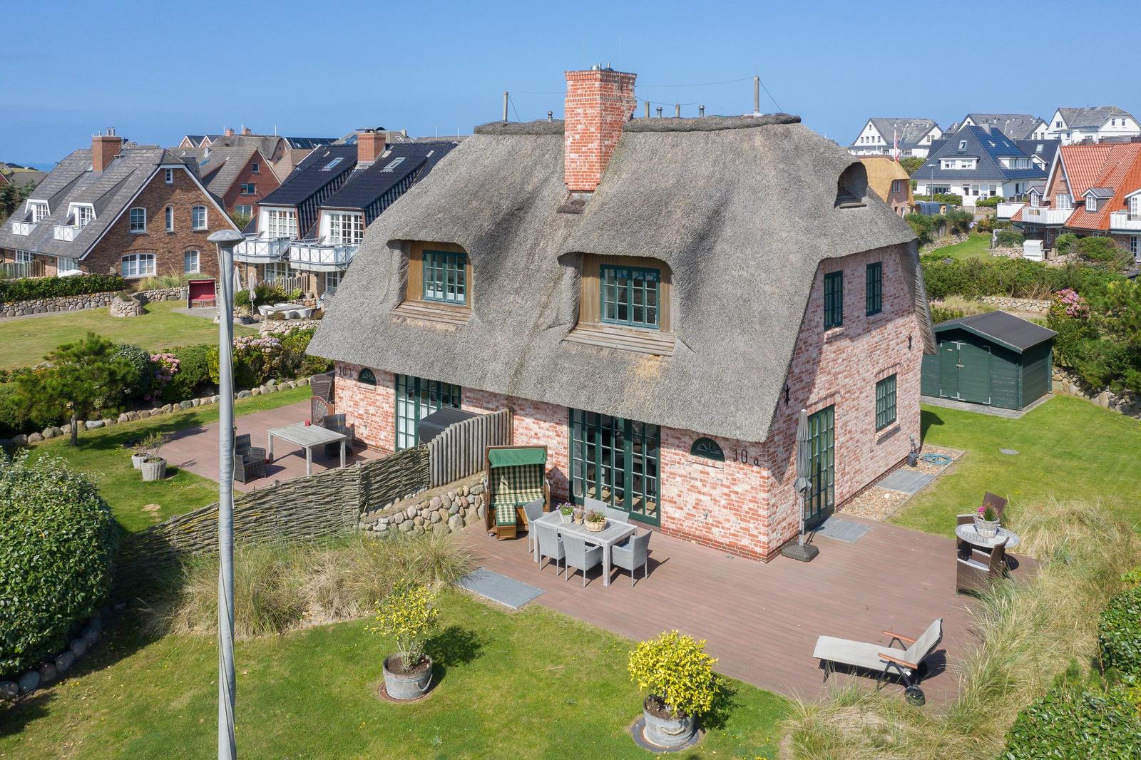 Dorfhaus mit Strohdach und Gartenbereich mit Terrasse.