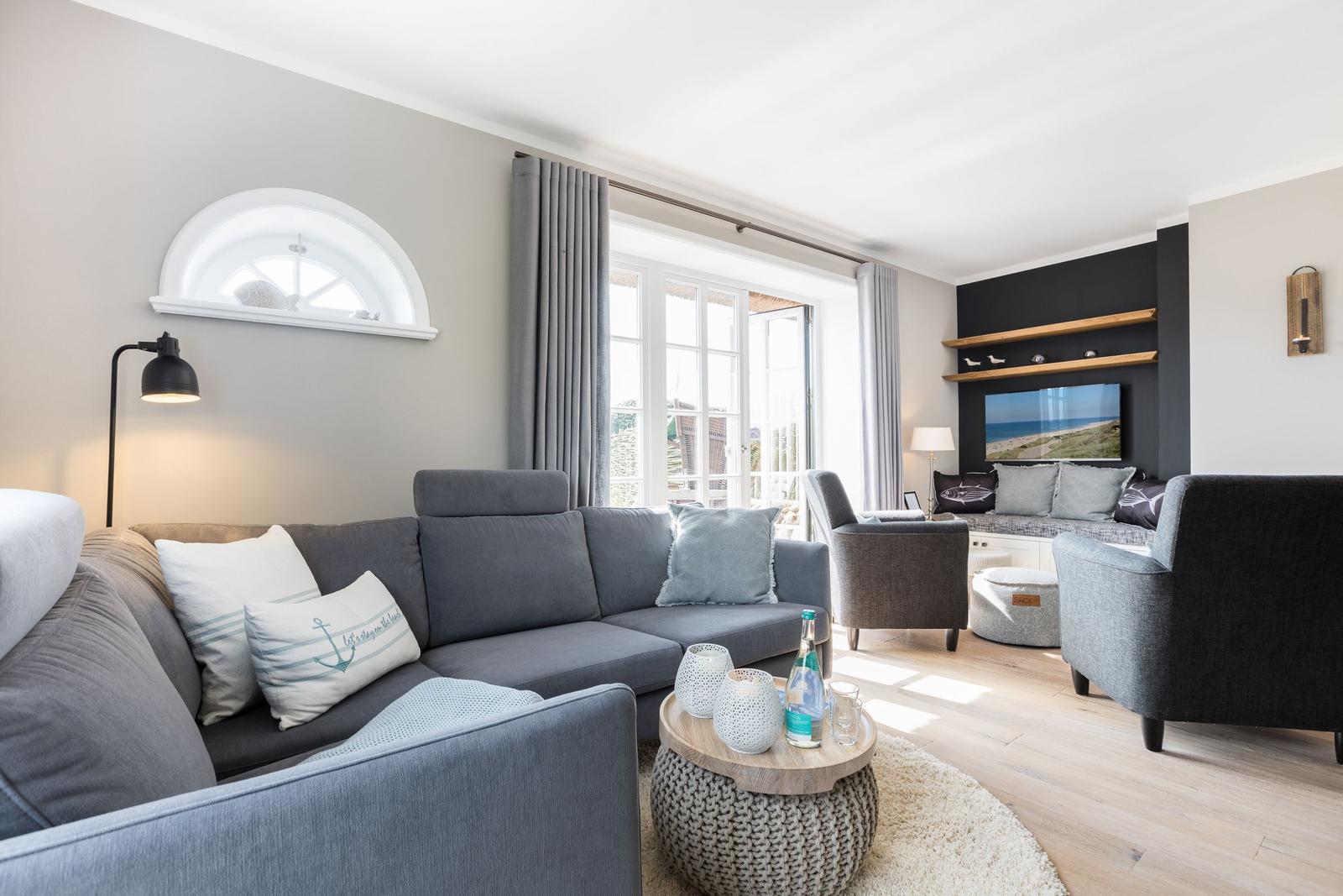 Wohnzimmer mit grauem Sofa, Fernseher und Blick auf Terrasse.