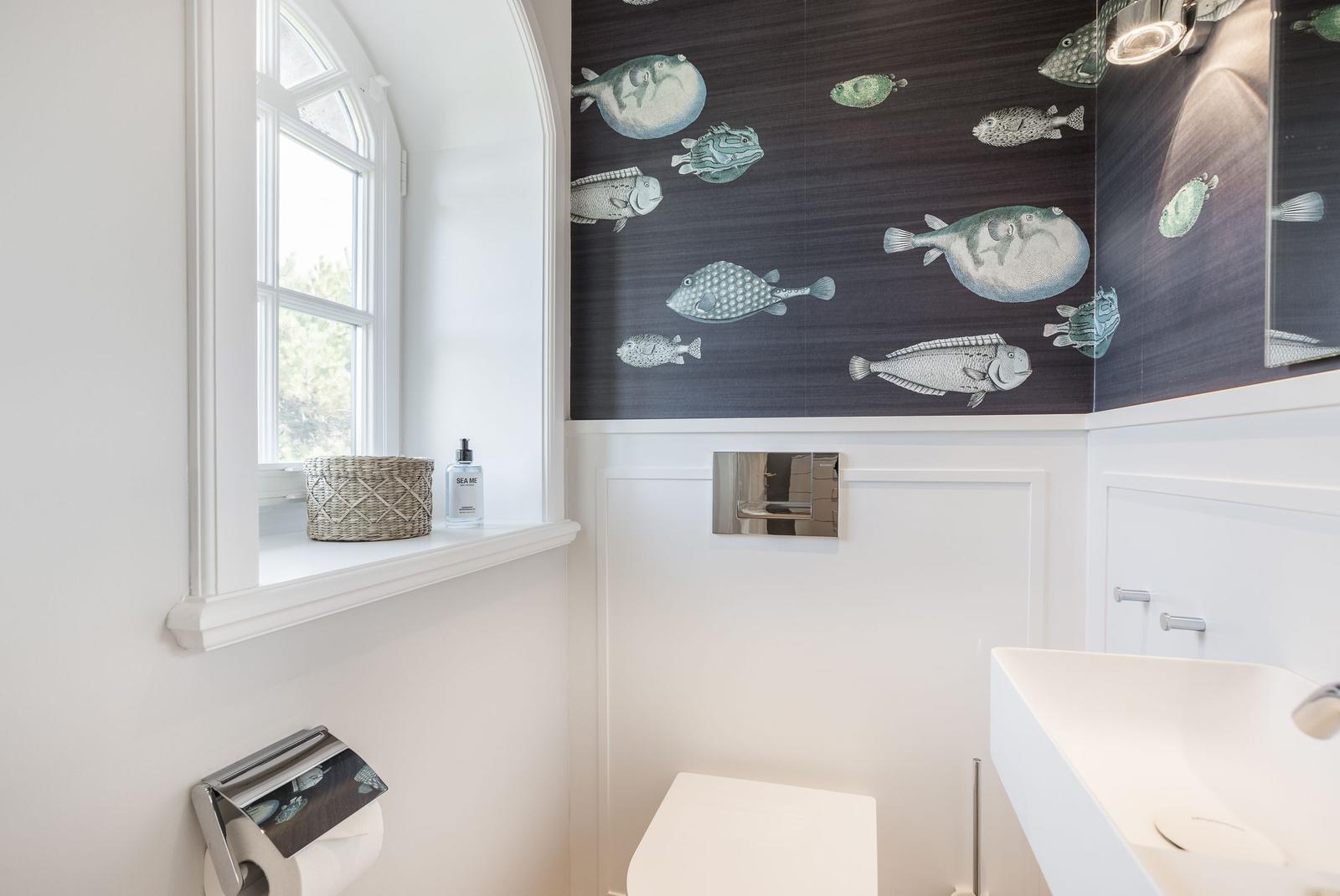 Badezimmer mit Fischmotiv-Wand, Fenster, Waschbecken und Toilette.