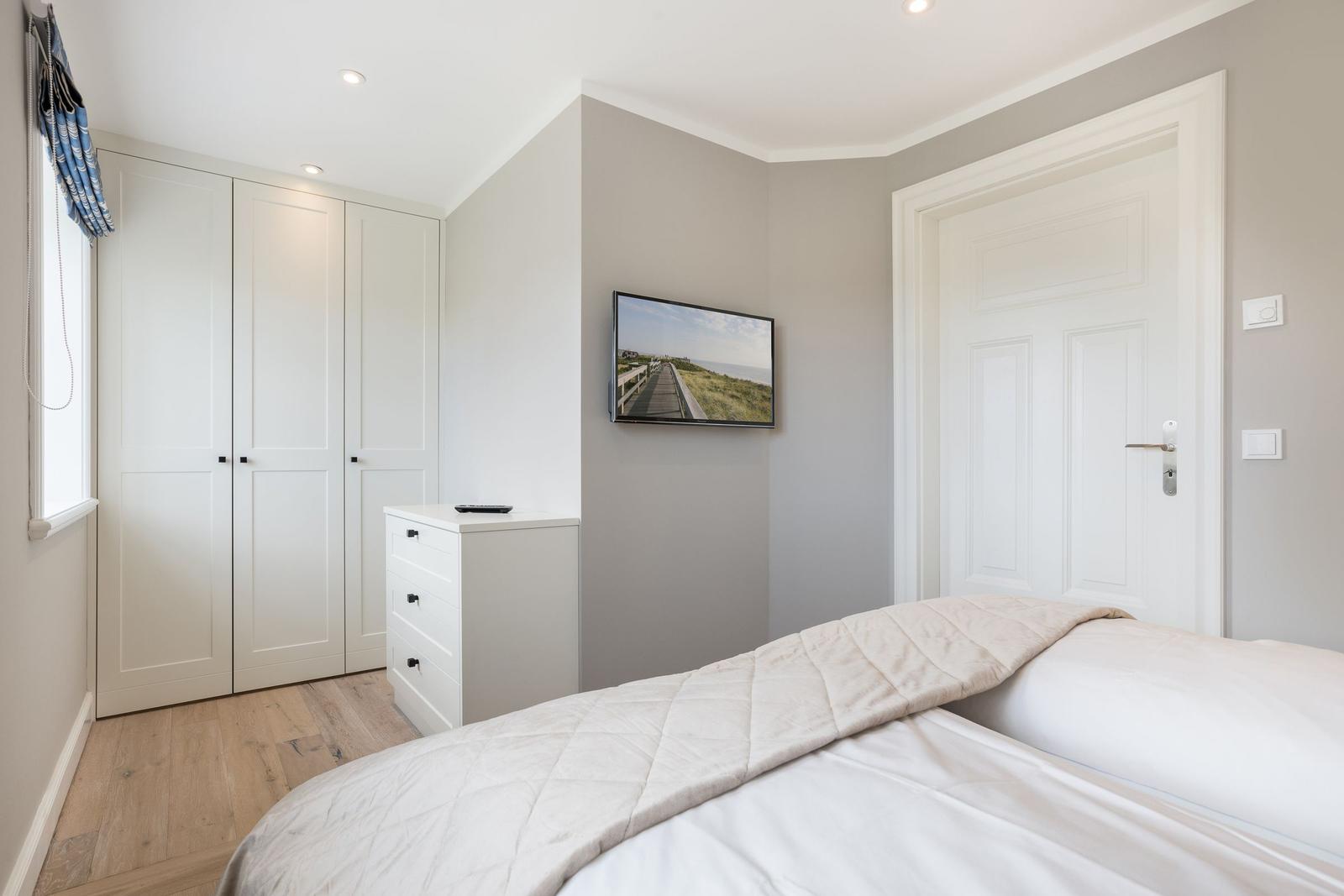 Schlafzimmer mit Bett, Kleiderschrank und Fernseher an der Wand.