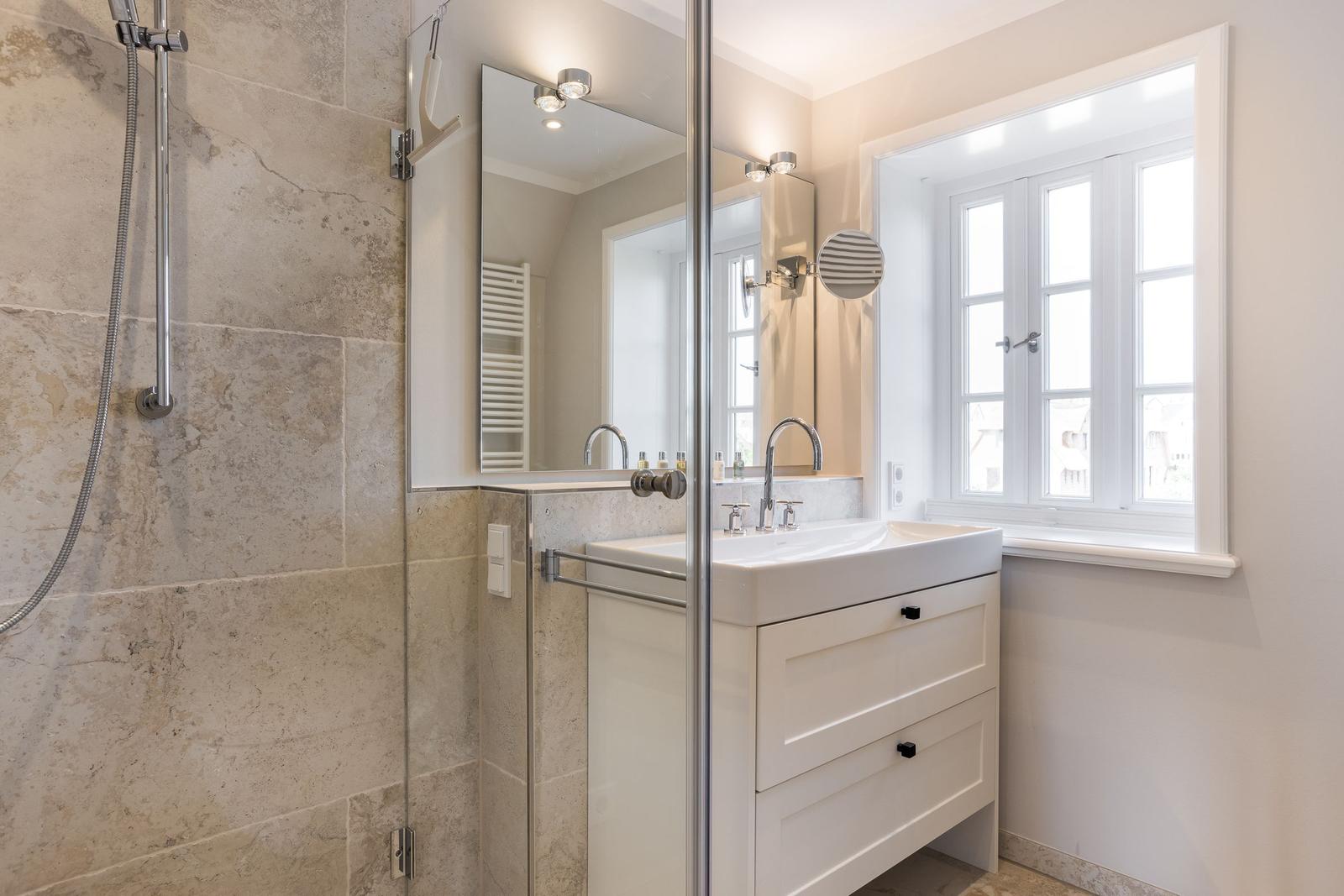 Badezimmer mit Dusche, Waschbecken und Fenster.