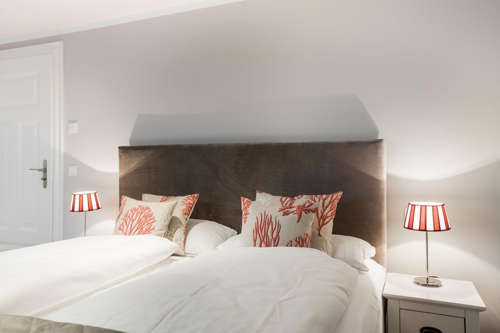 Schlafzimmer mit Bett, Kissen und Nachttischen mit Lampen.