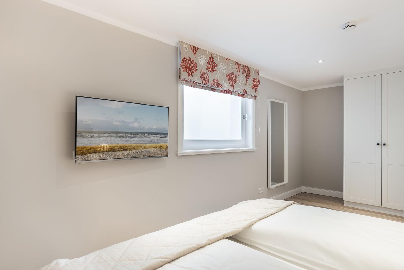 Schlafzimmer mit Bett, TV und Fenster mit Vorhang.