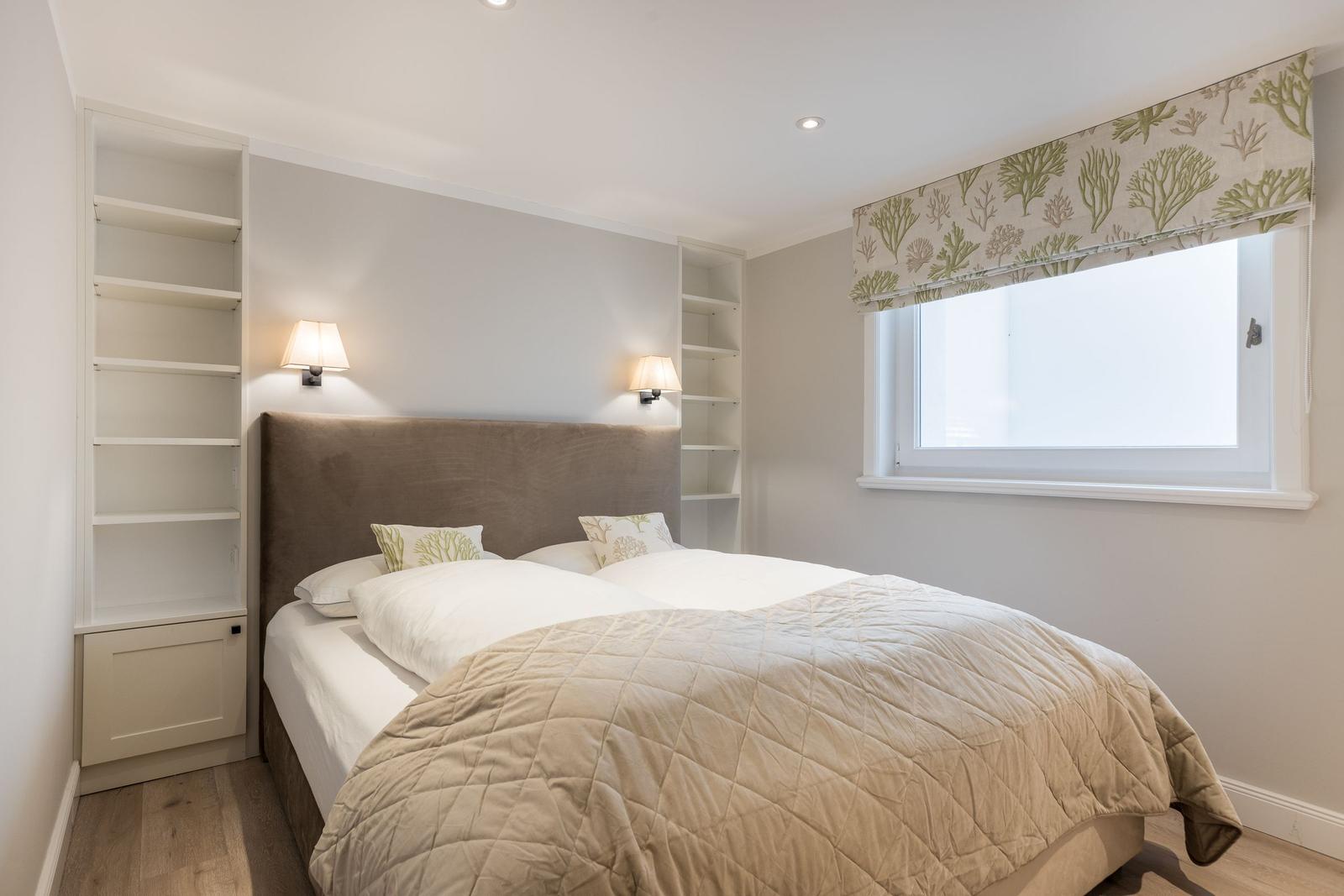 Schlafzimmer mit Bett, Fenster und eingebauten Regalen.