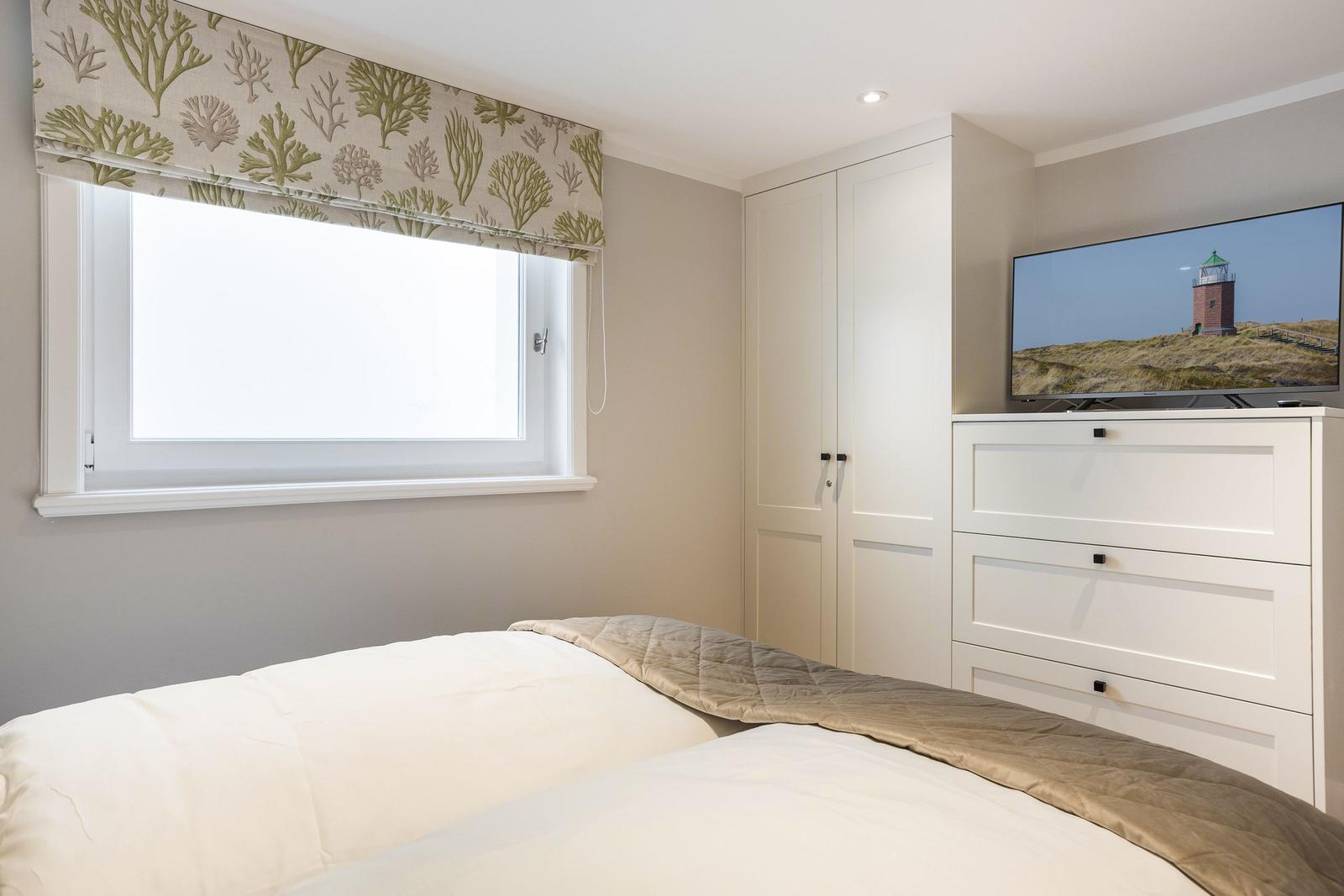 Schlafzimmer mit Bett, Schrank und Fernseher an der Wand.