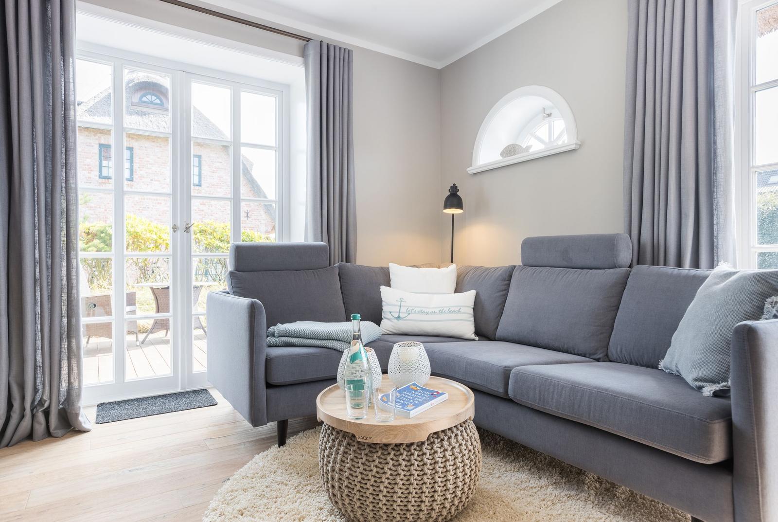 Ein Wohnzimmer mit grauem Sofa, Holzboden und Fenster zur Terrasse.
