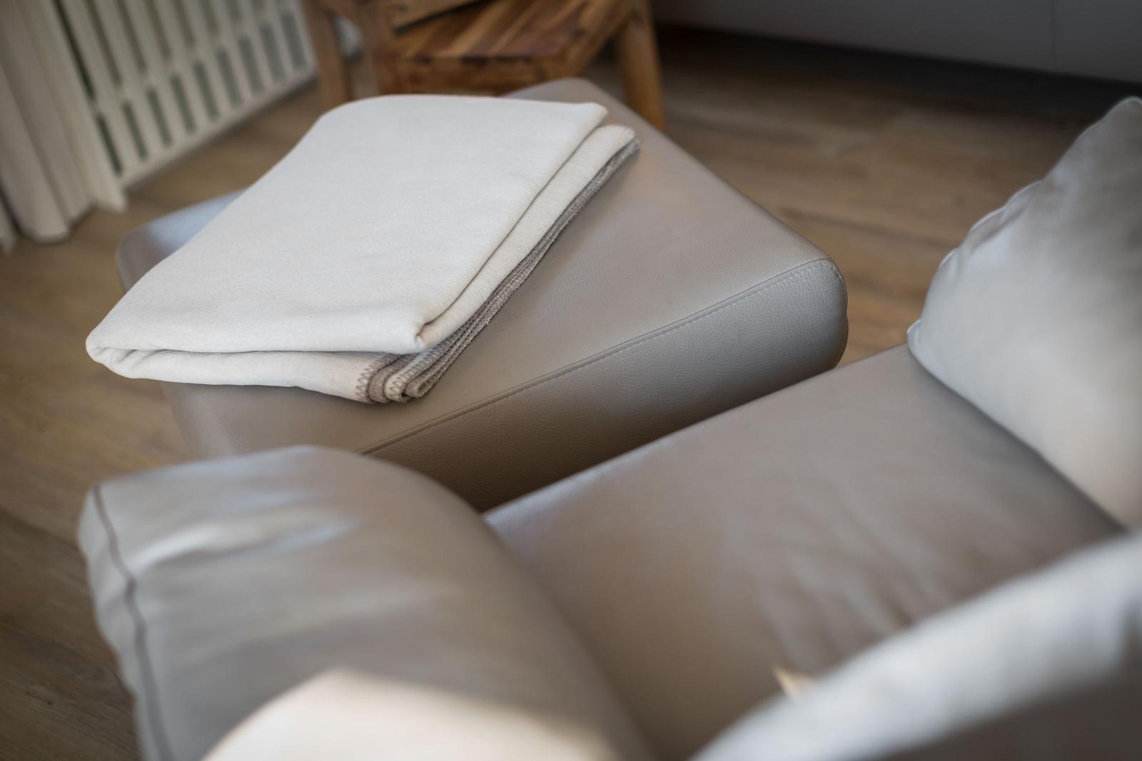 Graue Ledercouch mit gefaltetem Deckenbezug und Holzboden im Hintergrund.