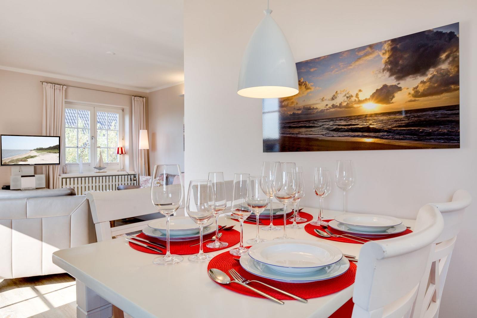 Esszimmer mit weißem Tisch, roten Untertellern und Wandbild von Sonnenuntergang.