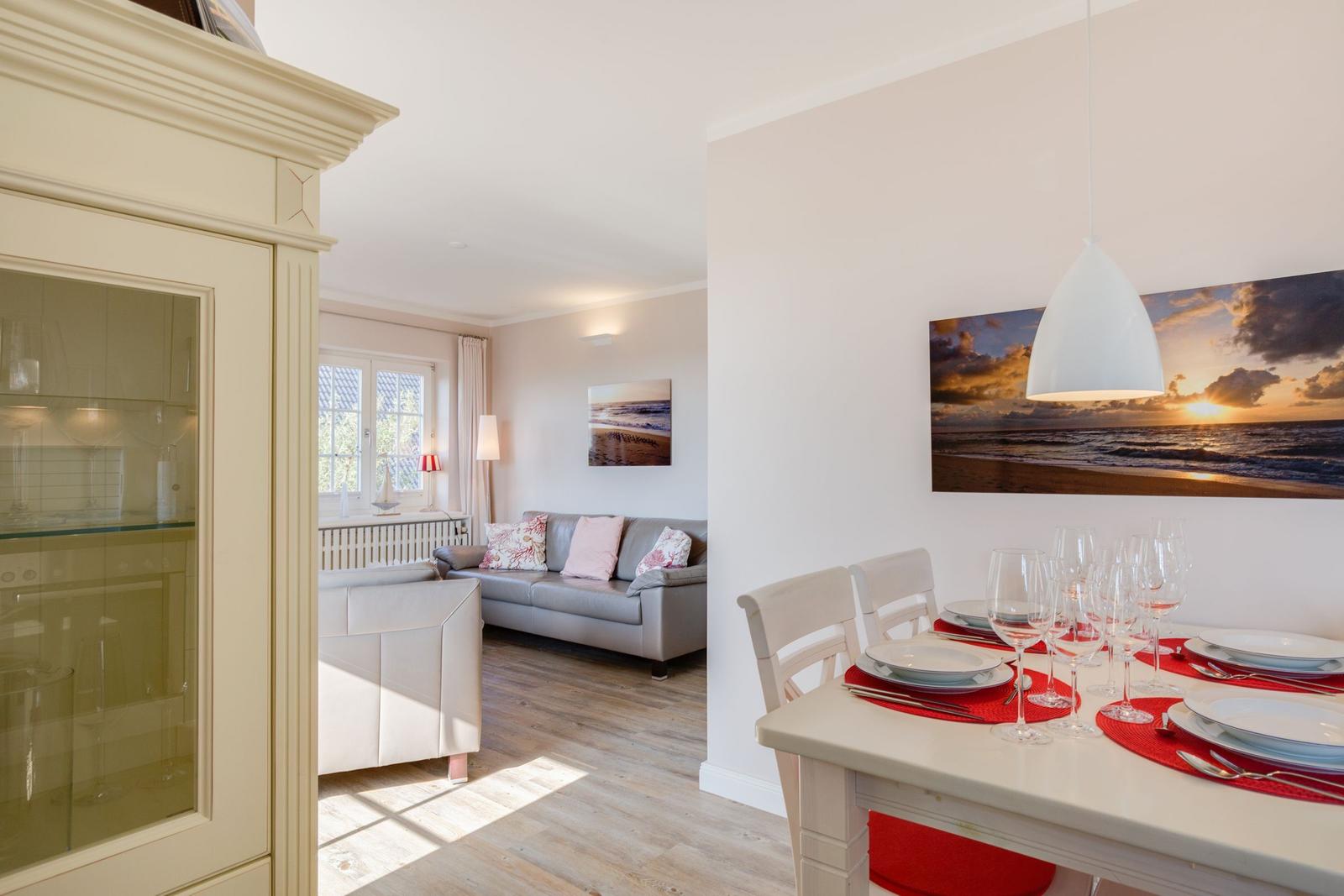 Essbereich mit Tisch und Stühlen. Wohnzimmer mit Sofa und Fenster. Wandbild zeigt Sonnenuntergang.