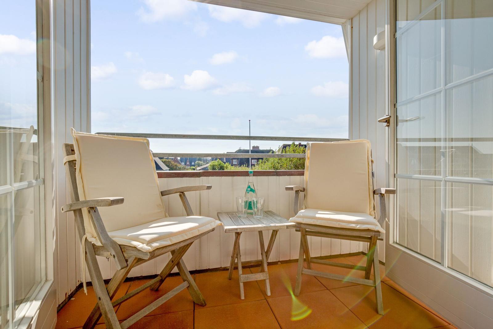 Balcony with two chairs and a table for two. View over rooftops and sky.