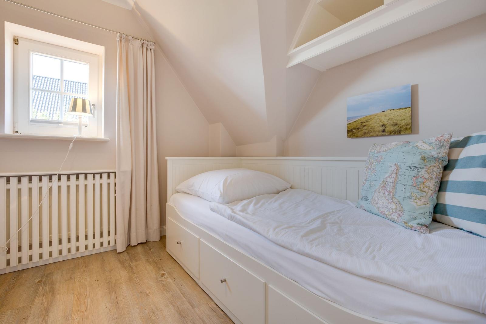 Schlafzimmer mit Dachschrägen, weißem Bett und Holzboden. Fenster mit Vorhang und Wandbild.