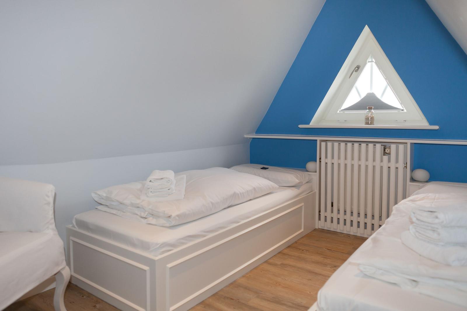 Zimmer mit zwei Betten, blauer Wand und Dreiecksfenster