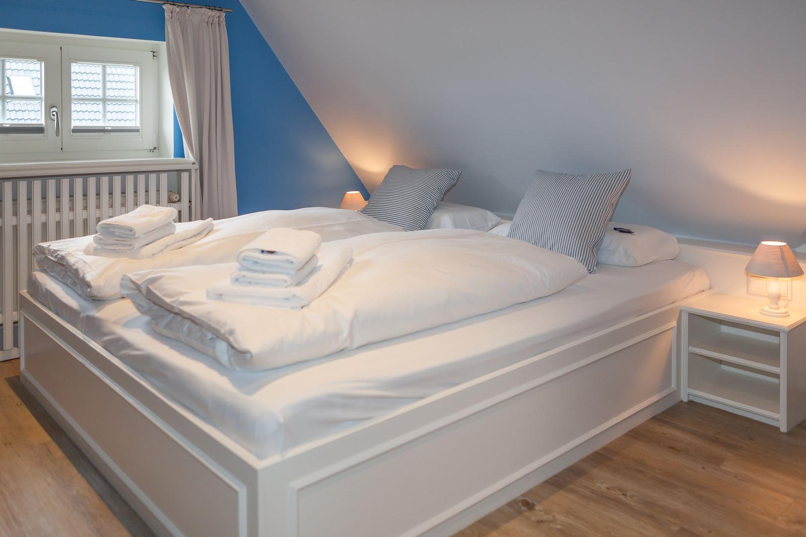 Schlafzimmer mit Doppelbett, Fenster und Nachttisch.