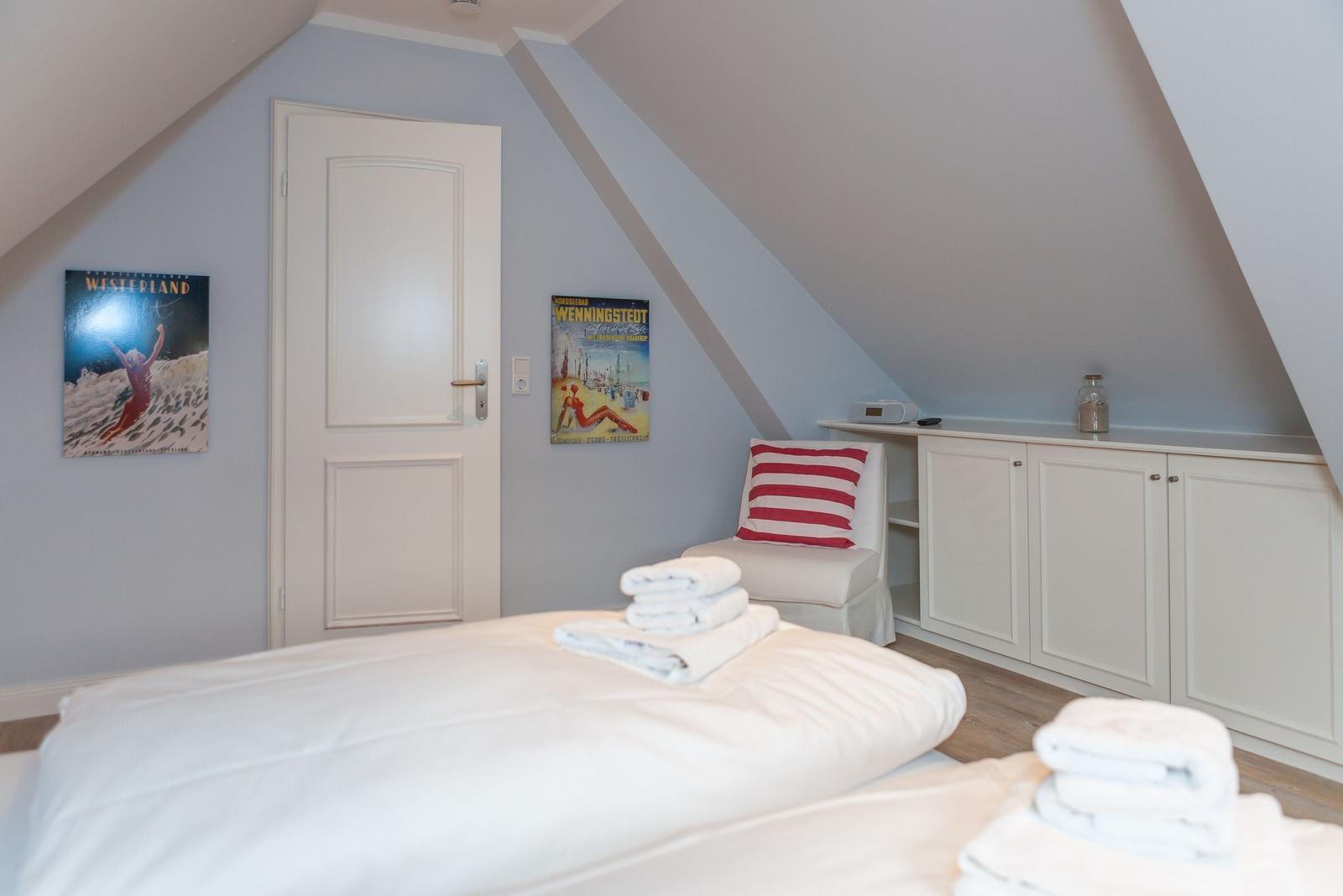 Schlafzimmer mit Dachschrägen, Bett, Stuhl und Schrank.