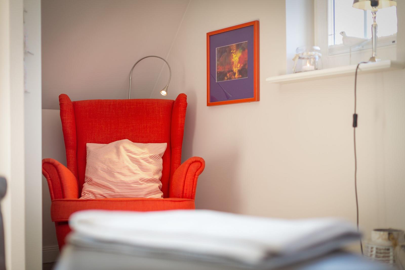 Rotes Sessel mit Kissen, Wandbild und Fensterbank mit Lampen.