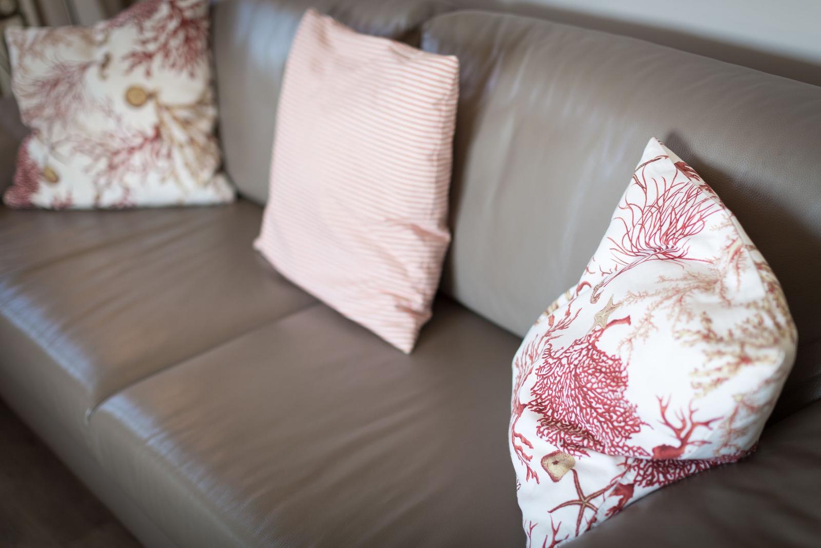 Ein Sofa mit drei Kissen, zwei mit Korallenmuster, eines mit Streifen.
