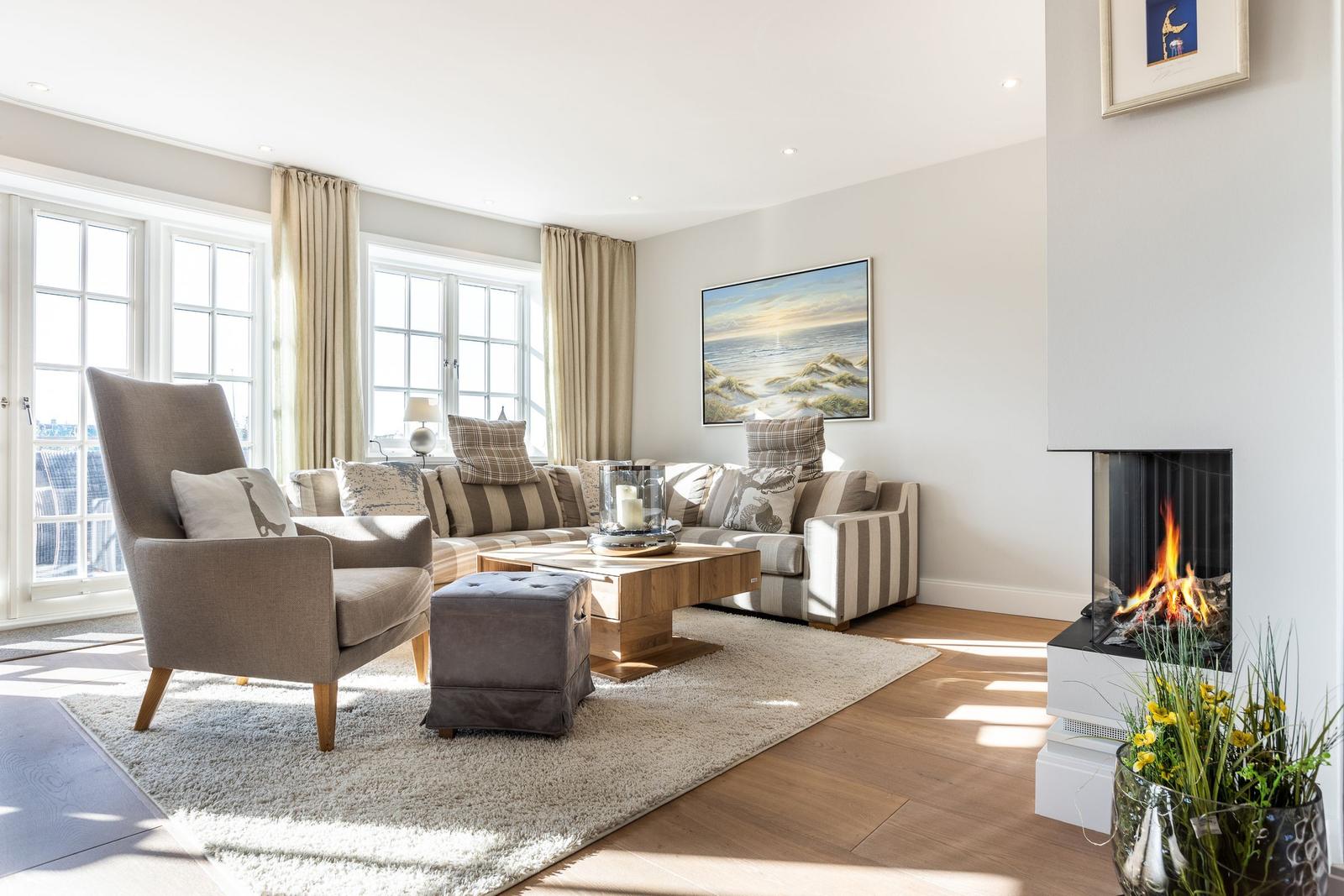 Living room with sofa, armchair, fireplace, and large windows.