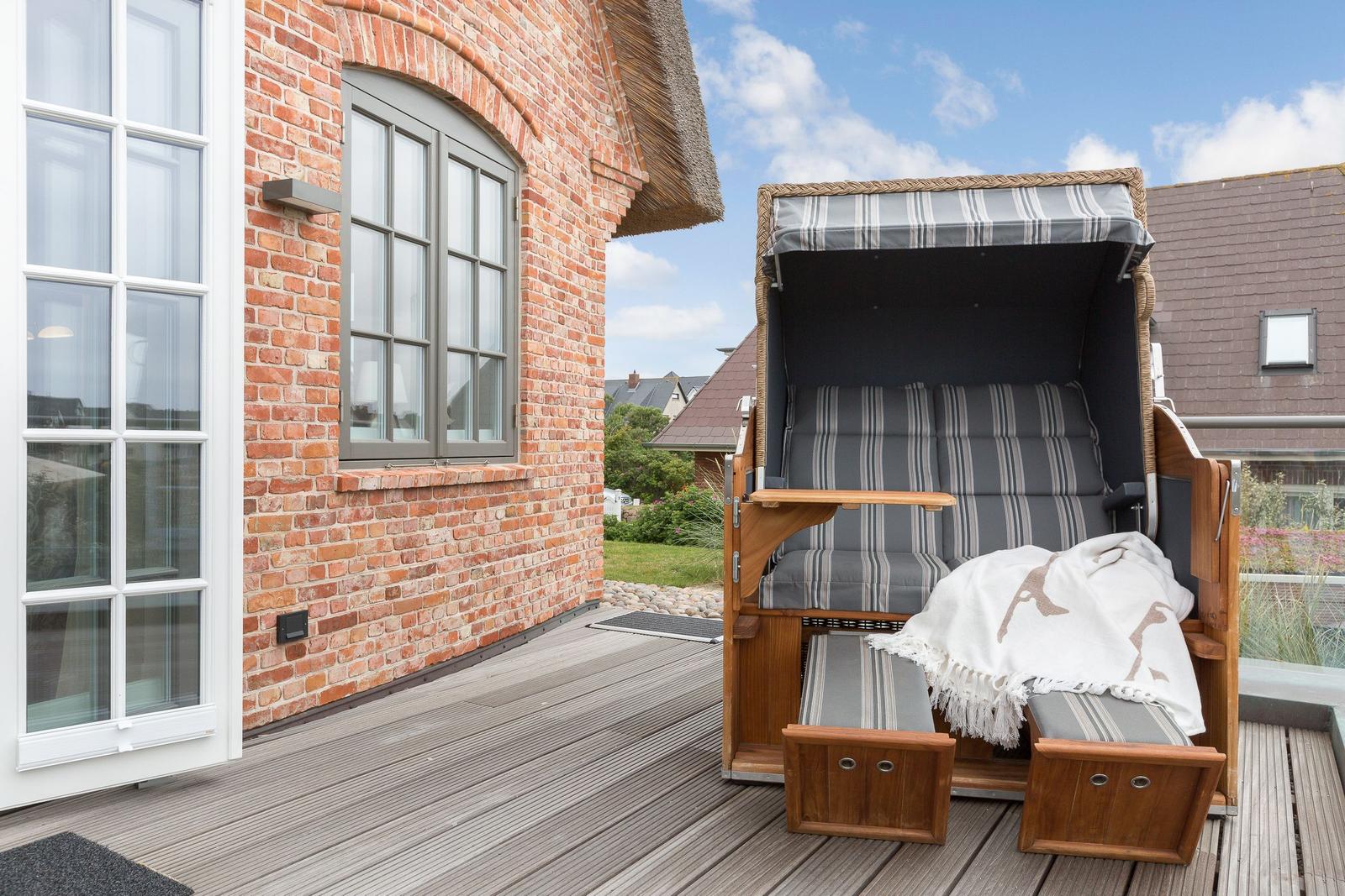 Deck with wicker lounge chair and wooden floor beside brick house