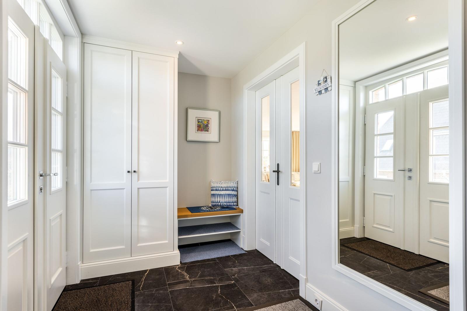 Entrance with shoe cabinet, bench, and mirror. White doors and dark tiles.