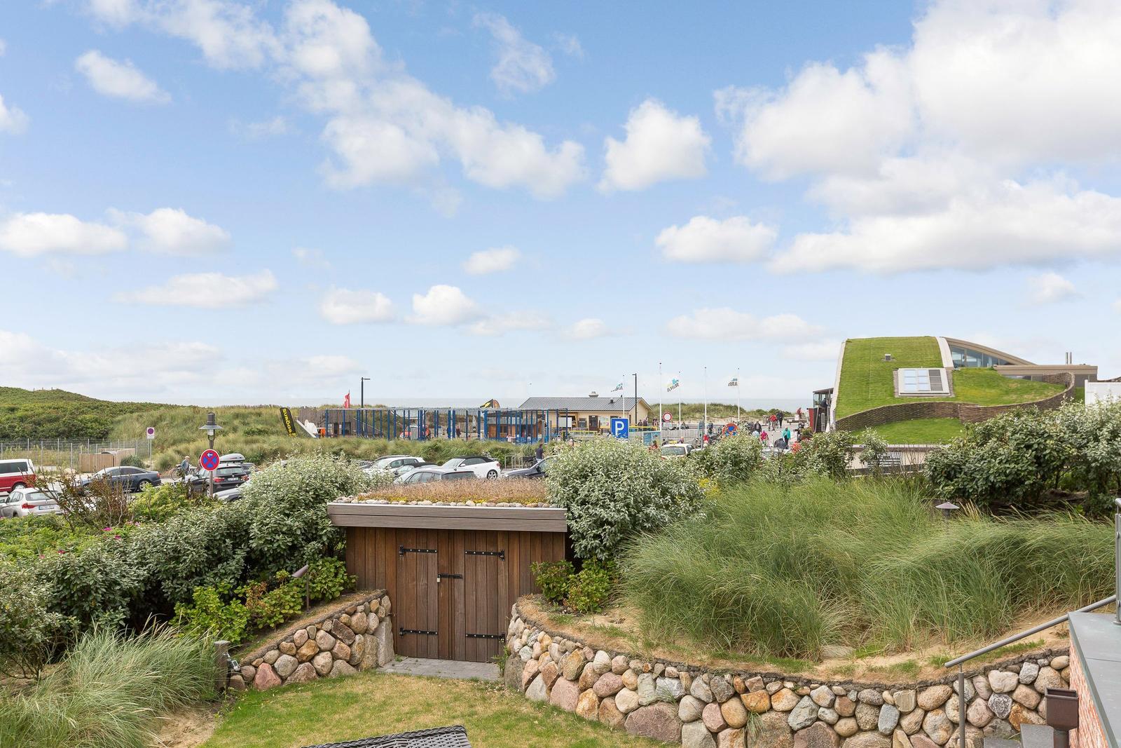 Green rooftop garden with stone walls and view of beach area.