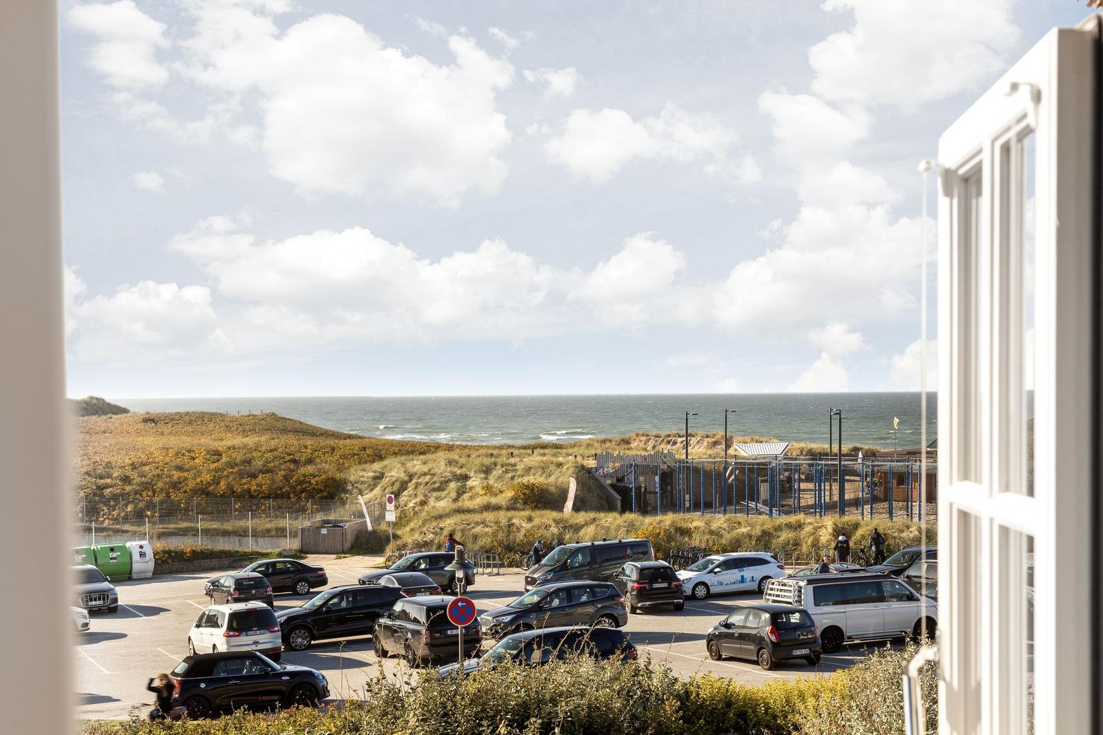 From the window, you see a parking lot with cars and the sea.
