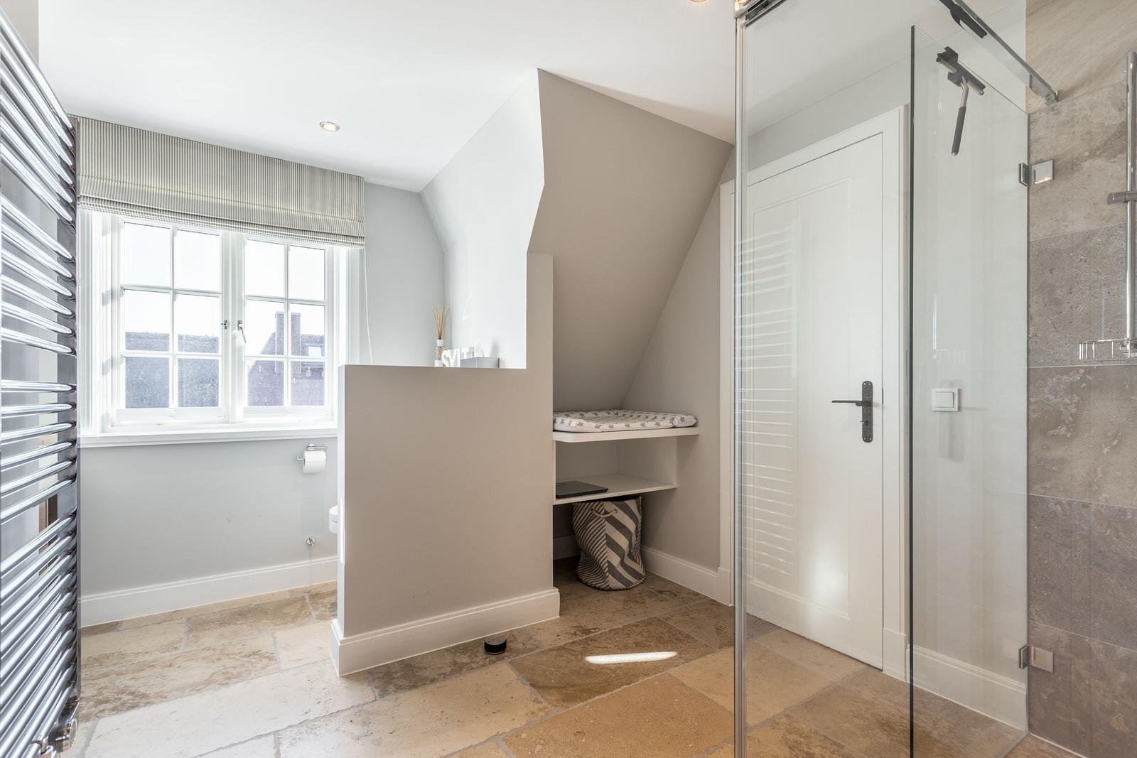 Bathroom with shower, window, and seating area under sloped ceiling.