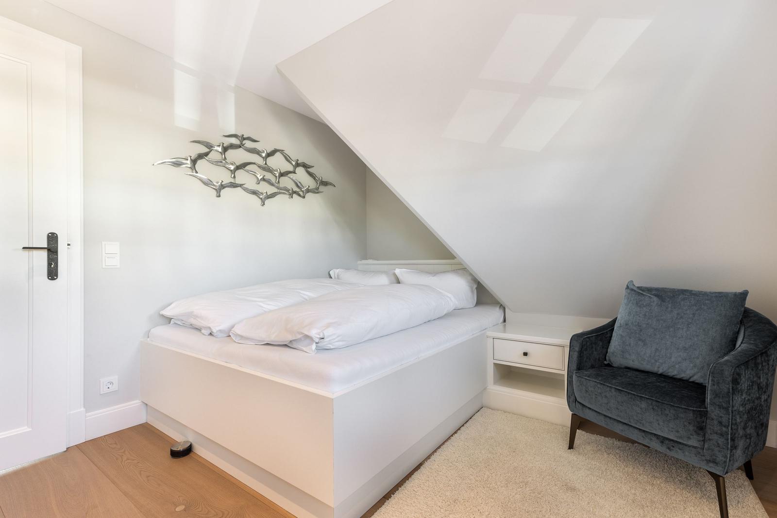 Bedroom with sloped ceiling, bed, and armchair.