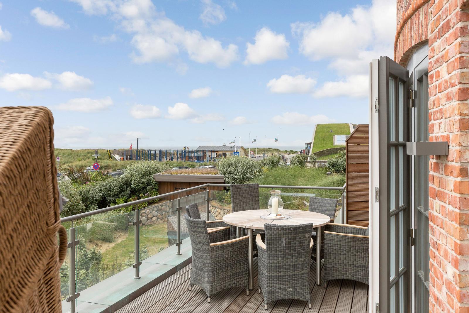Terrace with table and chairs, view of beach and green areas.