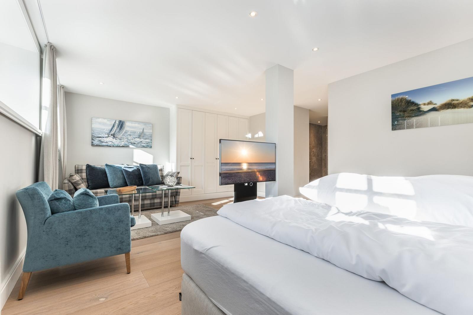 Bedroom with bed, TV, and seating. Wall art shows beach and sailboat.