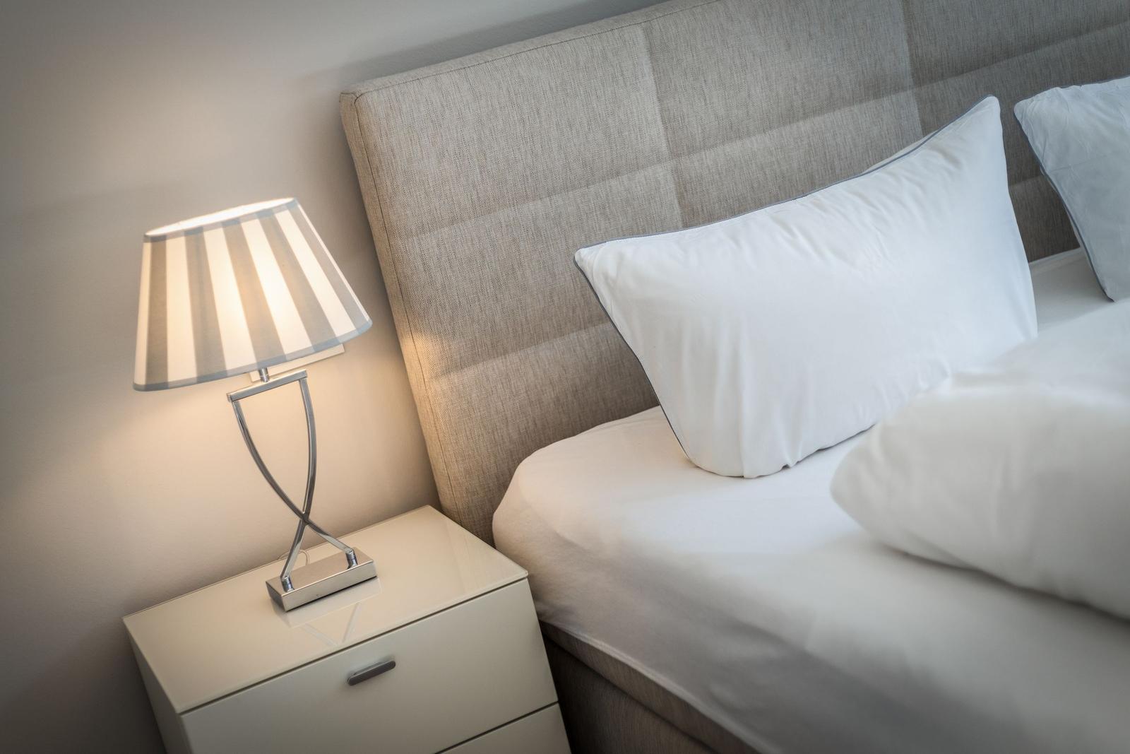 Bed headboard with white pillows and bedside table with lamp.