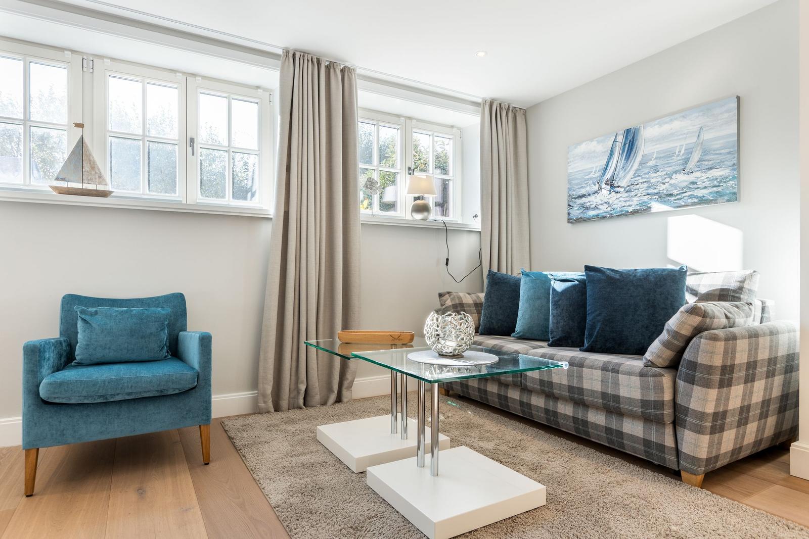 Living room with sofa, armchair, glass table, and wall art of sailboats.