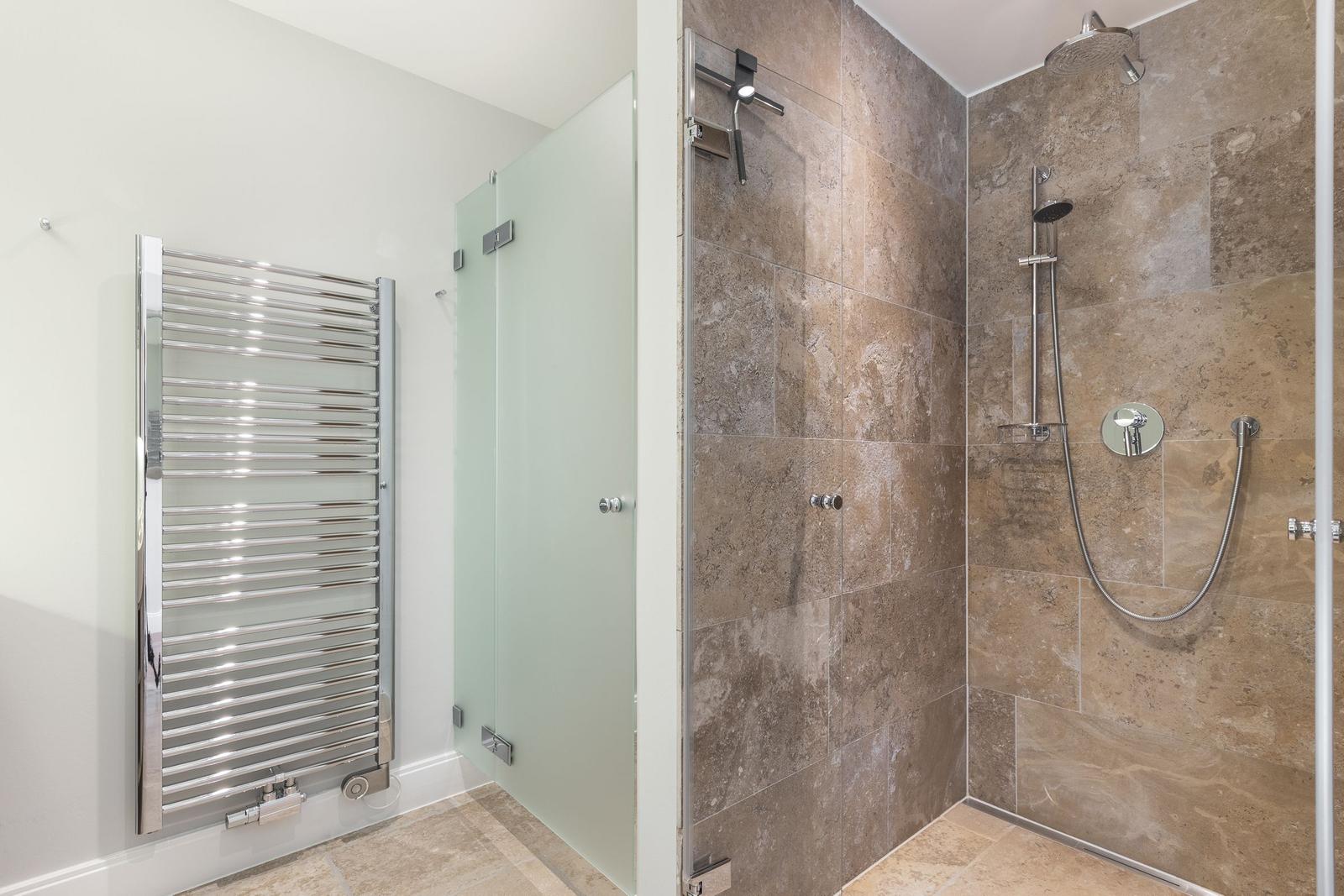 Shower with stone wall and handheld shower. Heater on the wall.
