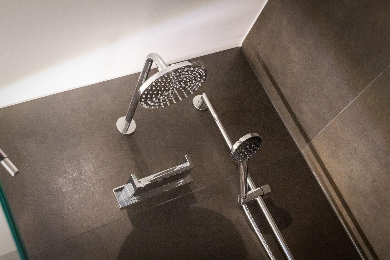 Shower with shower head and handheld shower on dark floor