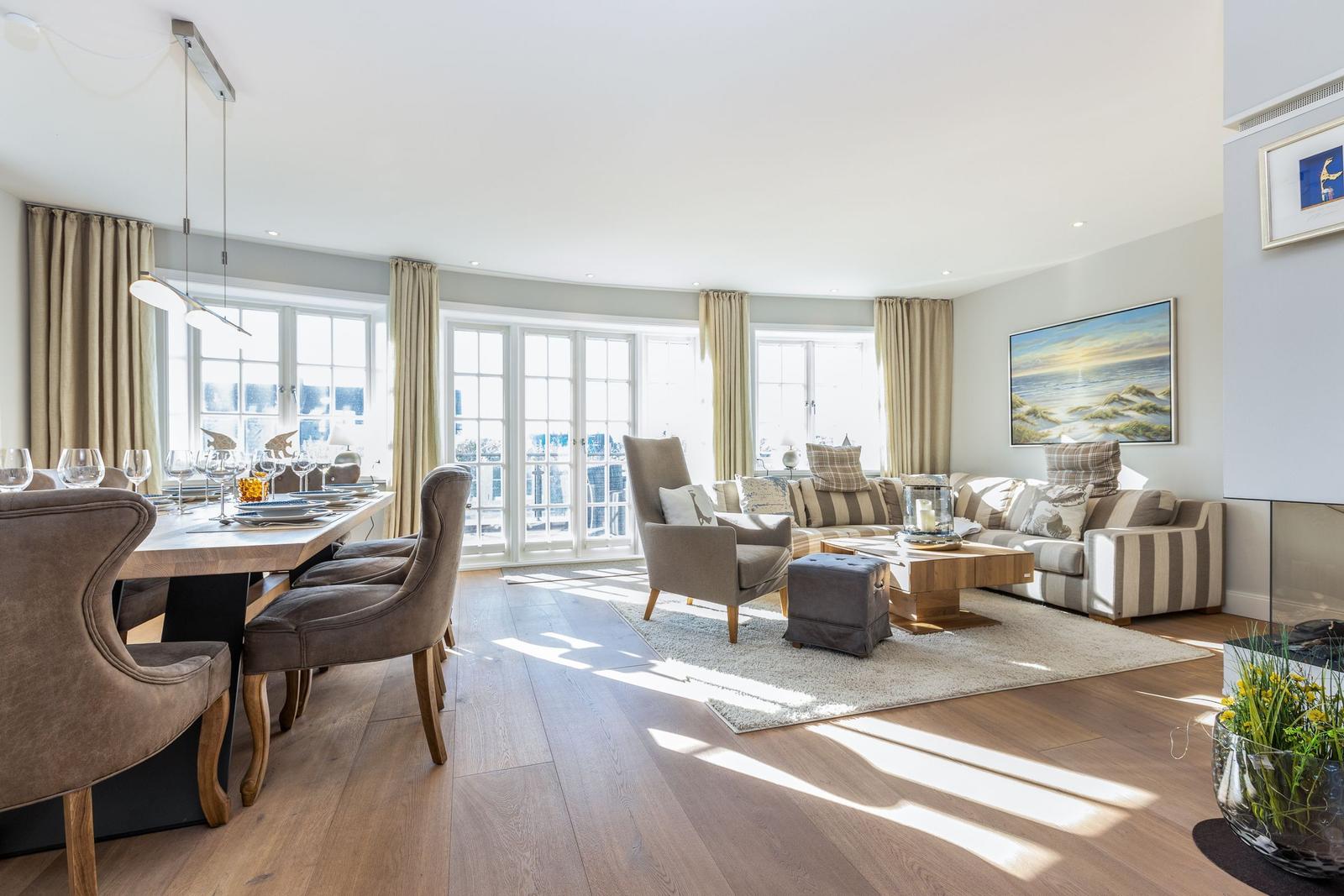 Living and dining area with wooden floor, sofa, table and chairs, large windows.